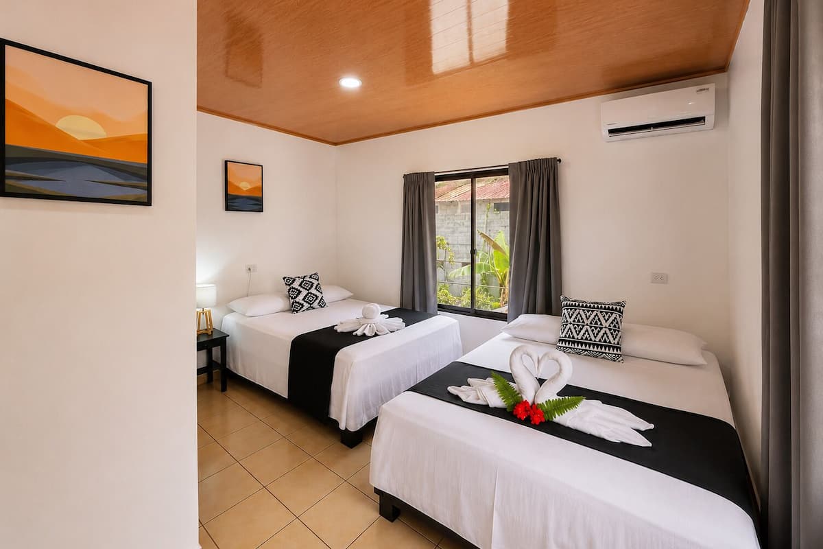 A hotel room with two beds, a window with curtains, an air conditioning unit, and artwork on the walls.