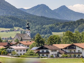 A village with traditional houses, a church with a bell tower, and mountains in the background.