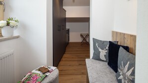 A narrow hallway with a wooden floor, a white radiator, a white shelf with a vase of flowers, and a grey sofa with decorative pillows. - Appartement 4 "rauschberg" für 2 Personen, 32 m² (Inzell)