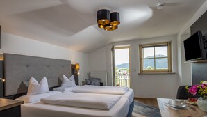 A hotel room with two beds, a desk, a dining table with a cake, a TV, and a window with a view of the mountains. - Appartement 4 "rauschberg" für 2 Personen, 32 m² (Inzell)