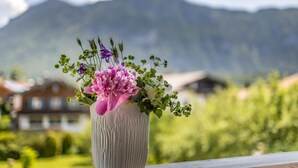 A white vase with a floral arrangement on a balcony overlooking a mountainous landscape.