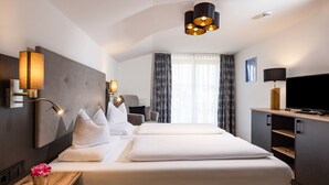 A modern hotel room with a large bed, a desk with a lamp, a television, and a chair.