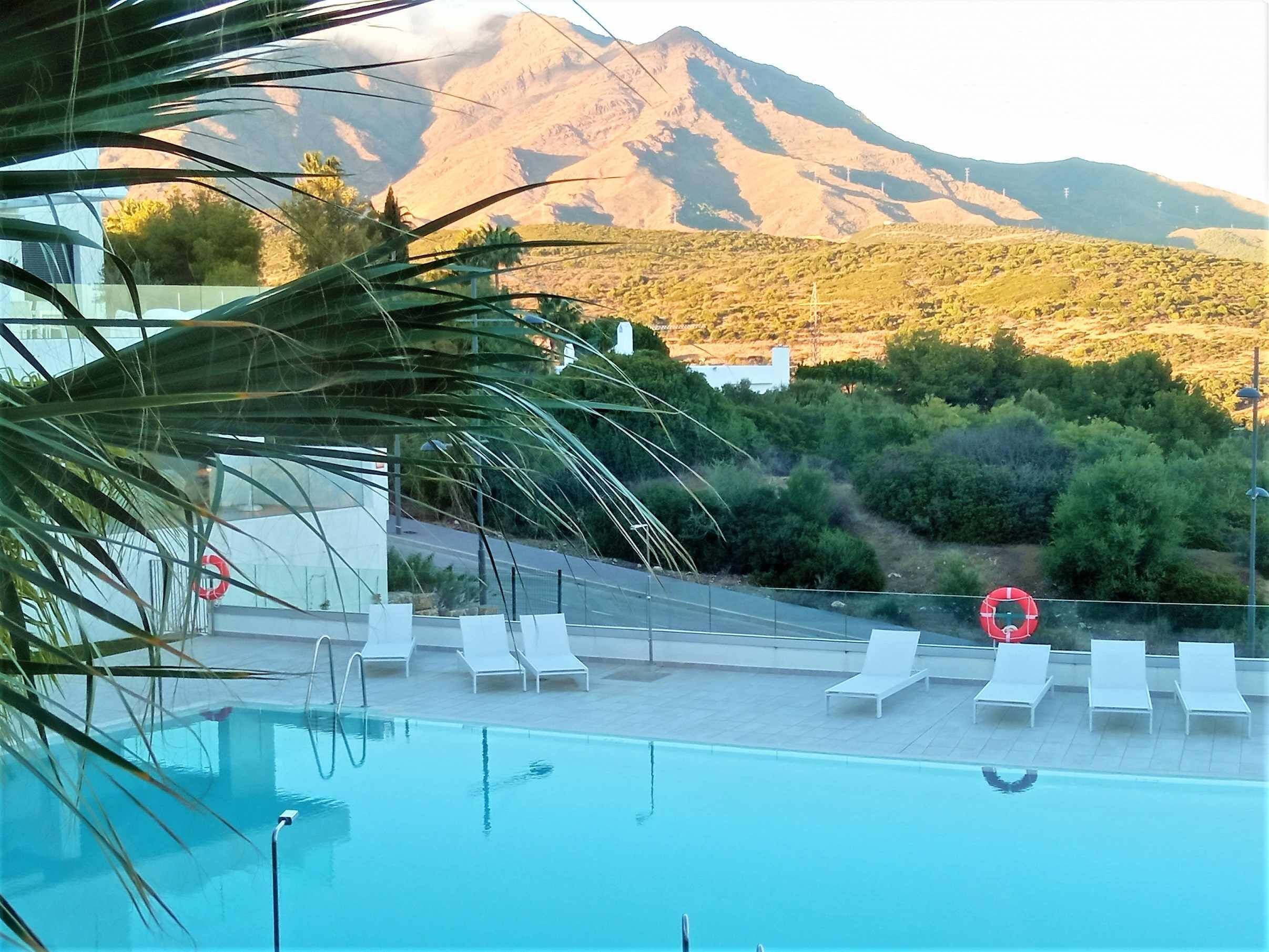 A pool with lounge chairs and a lifebuoy, overlooking a mountainous landscape.