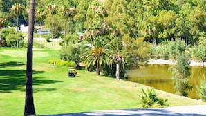 Un parcours de golf avec un étang, des palmiers et une chaîne de montagnes en arrière-plan.