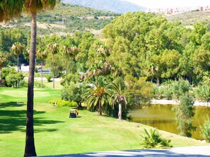 Un campo de golf con un estanque, palmeras y montañas al fondo.