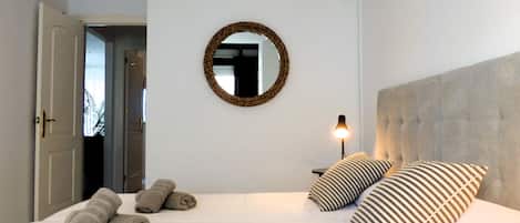 Un dormitorio con una cama, dos almohadas, una lámpara de noche, un espejo y una puerta.