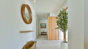Een moderne gang met een houten deur, een plant in pot, een geweven mand en een spiegel aan de muur.
