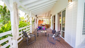 A covered outdoor patio with a wooden deck, white railings, and a seating area with two chairs and a table. - Villa Familiale Avec Piscine Privée à 5 Minutes de la Plage! (Sainte-Rose)