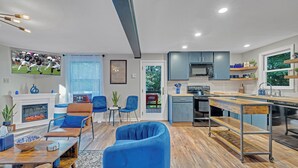 A modern living room with a fireplace, blue sofas, and a kitchen area with a dishwasher and microwave.