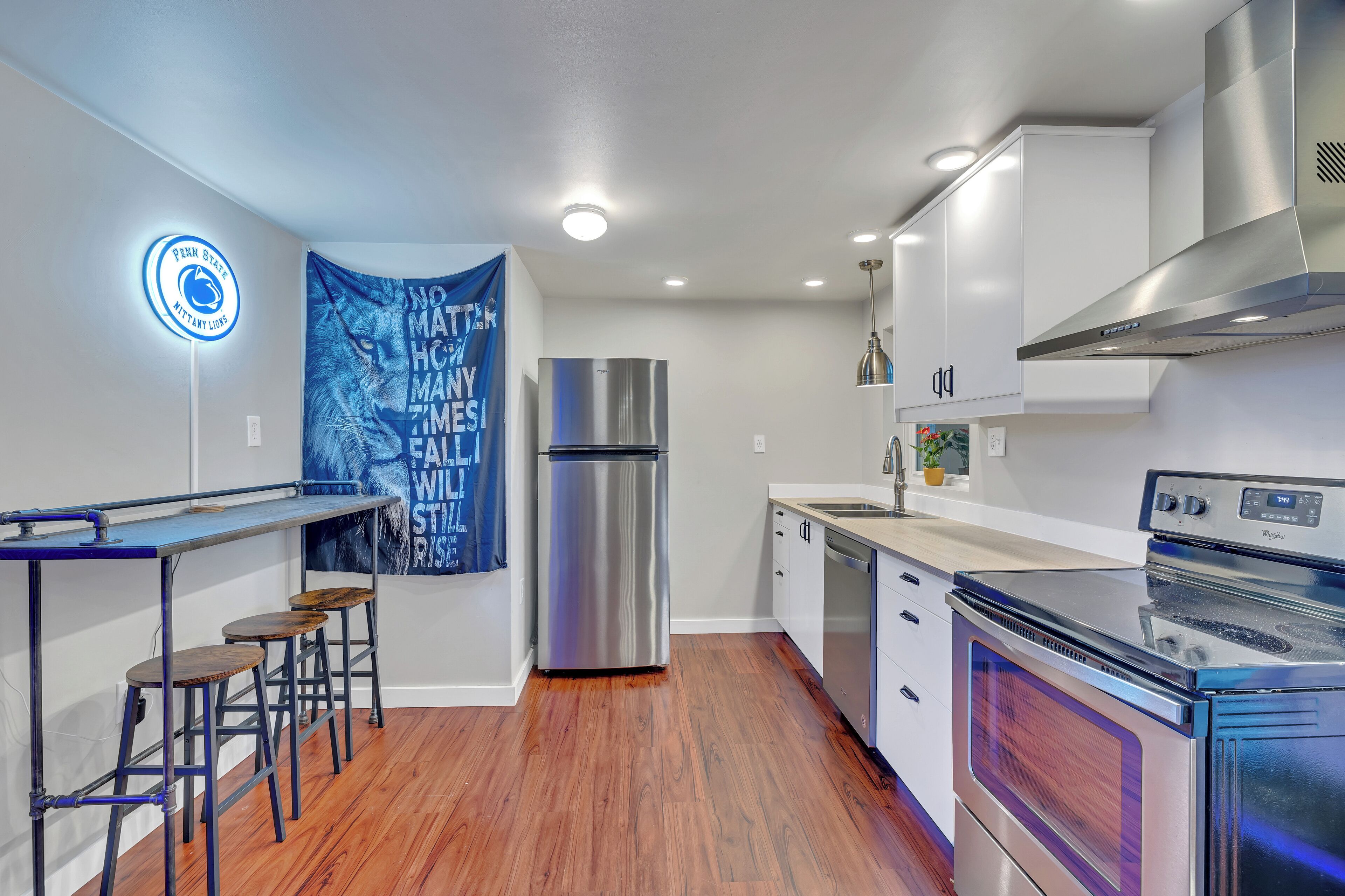 A modern kitchen with stainless steel appliances, wooden bar stools, and a stainless steel refrigerator.
