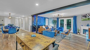 A modern living room with a wooden dining table, blue chairs, a sofa, and a fireplace.
