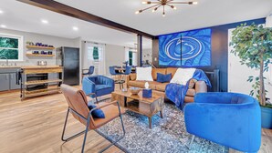 A modern living room with a sofa, chairs, a coffee table, and a large blue wall art piece.
