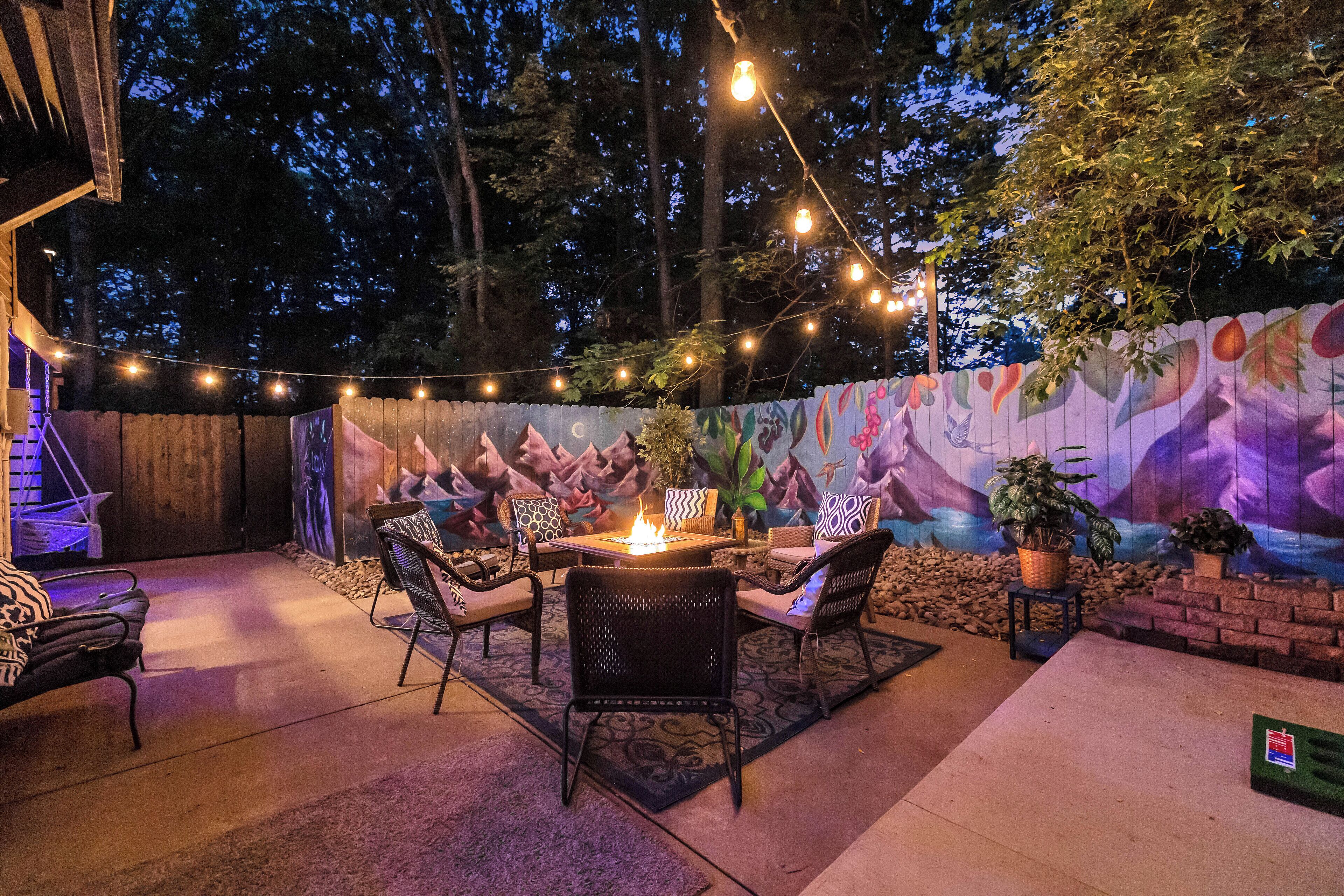 Een terras buiten met een vuurkuil, zitplaatsen en sfeerverlichting.