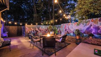 Een terras buiten met een vuurkuil, zitplaatsen en sfeerverlichting.