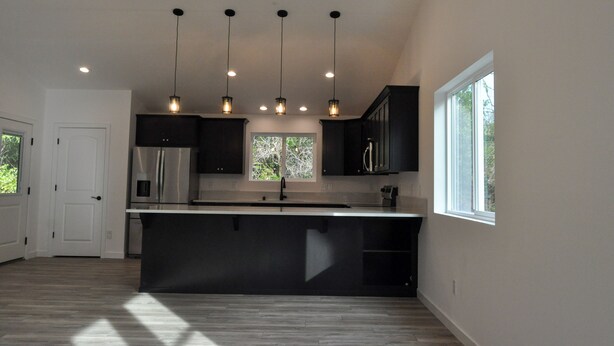 A modern kitchen with a central island, pendant lighting, and a view of the outdoors through a window.
