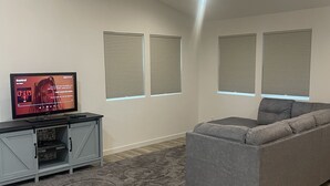 A modern living room with a grey sofa, a flat-screen TV on a grey cabinet, and a patterned rug.