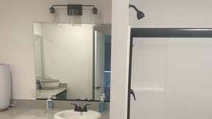 A modern bathroom with a white sink, dark cabinets, a large mirror, and a glass-enclosed shower.