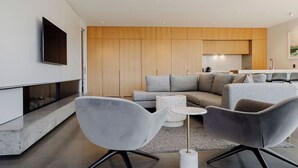 A modern living room with a sectional sofa, two grey armchairs, a small round coffee table, and a flat-screen TV mounted on the wall. - 3 min to The Remarkables / Lakefront Spa Luxury (Kawarau Falls)