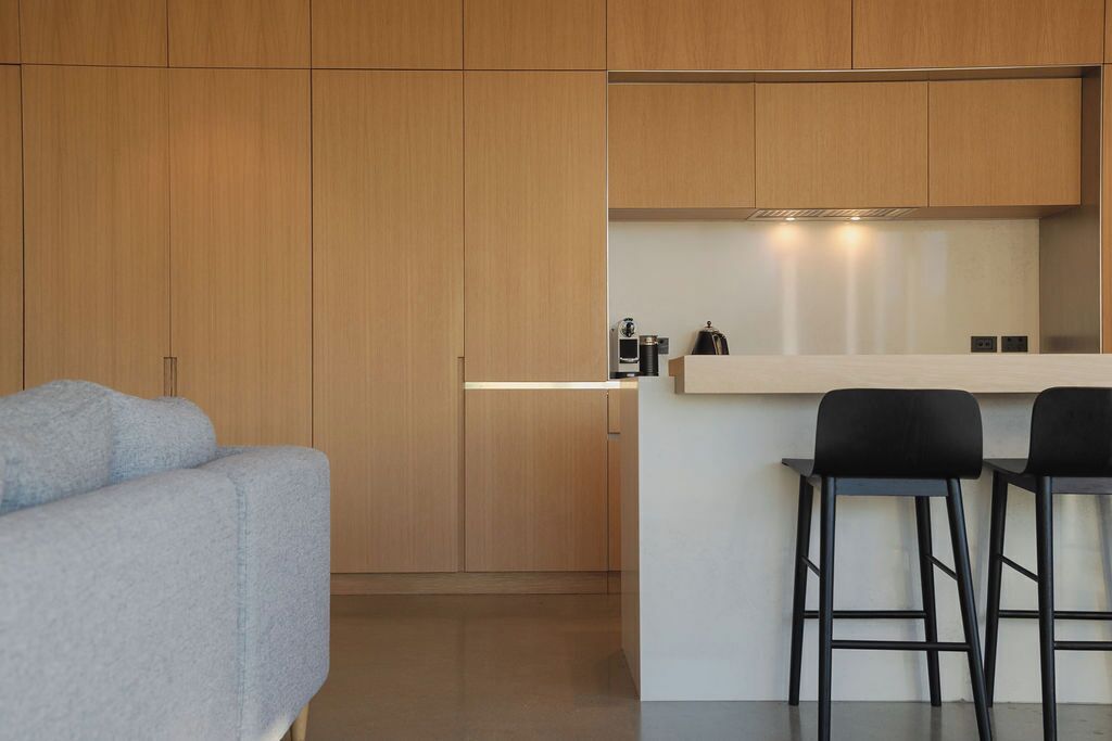 A modern kitchen with wooden cabinets, a white countertop, and two black bar stools.