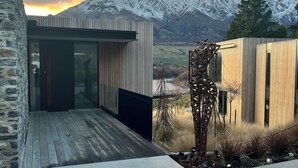 A modern building with a wooden deck and glass doors, set against a backdrop of snow-capped mountains and a clear sky. - 3 min to The Remarkables / Lakefront Spa Luxury (Kawarau Falls)