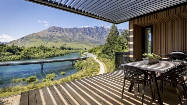 A wooden deck with a table and chairs, overlooking a river and mountains. - 3 min to The Remarkables / Lakefront Spa Luxury (Kawarau Falls)