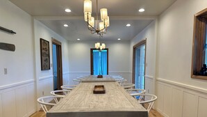 A long dining table with white chairs, a chandelier, and a wooden floor.