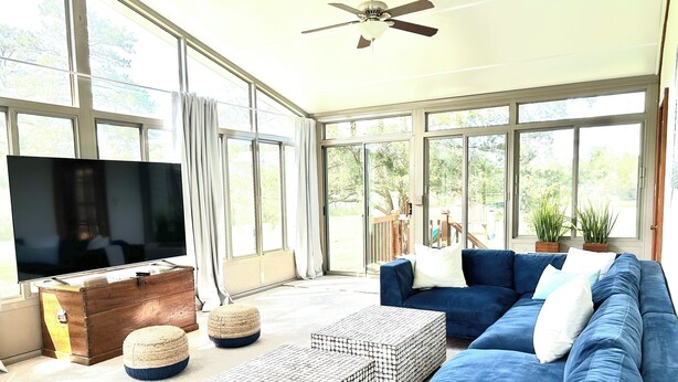 A spacious living room with a large TV, blue sofa, and a ceiling fan.