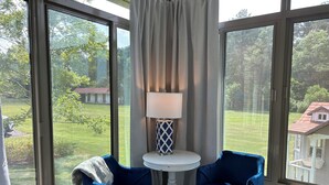A room with large windows, two blue chairs, a white table, and a lamp.