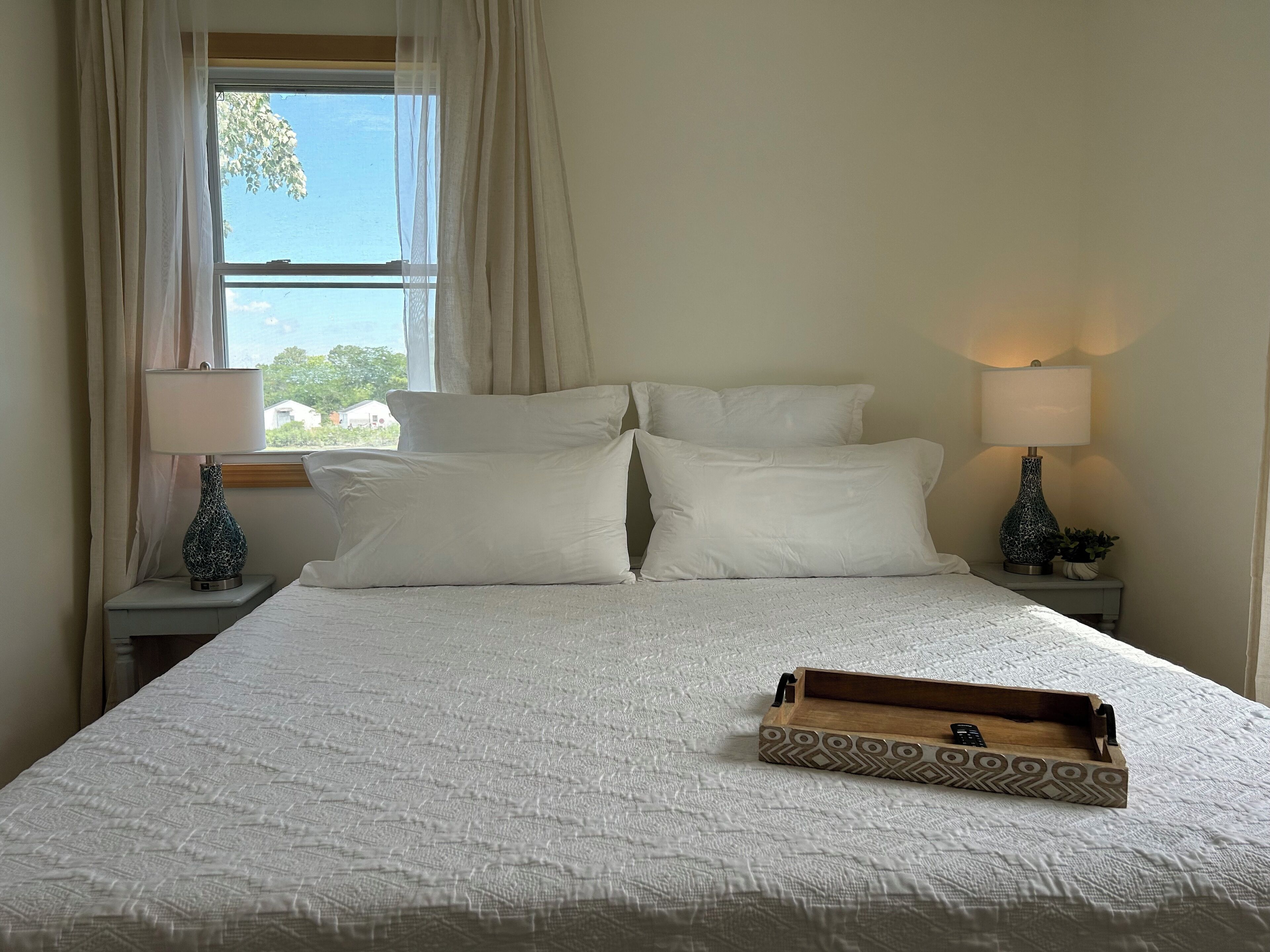 A neatly made bed with white bedding, two bedside lamps, and a wooden tray on the bed.