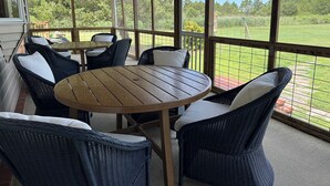 A covered patio with wicker furniture and a wooden table, overlooking a grassy yard.