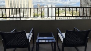 Ein Balkon mit drei Stühlen und einem kleinen Tisch, mit Blick auf eine Skyline aus hohen Gebäuden und einem klaren Himmel.