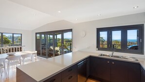 Une cuisine moderne dotée d’un grand îlot central, de meubles de rangement aux couleurs sombres et offrant une vue sur l’extérieur grâce à de grandes fenêtres.