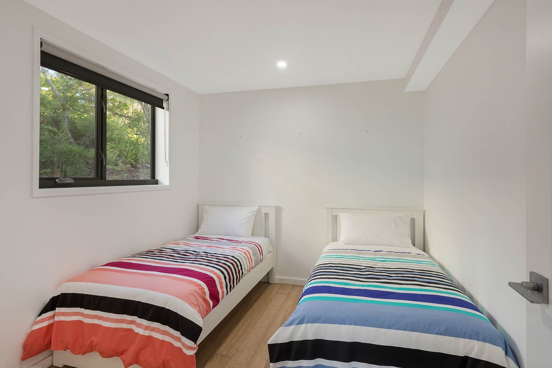 Una habitación pequeña y luminosa con dos camas individuales, una ventana que da a zonas verdes y un techo blanco.