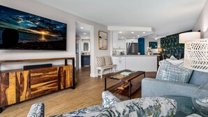 Un salon moderne doté d’un grand téléviseur à écran plat, d’un meuble de rangement en bois, d’un canapé bleu et d’une table basse.