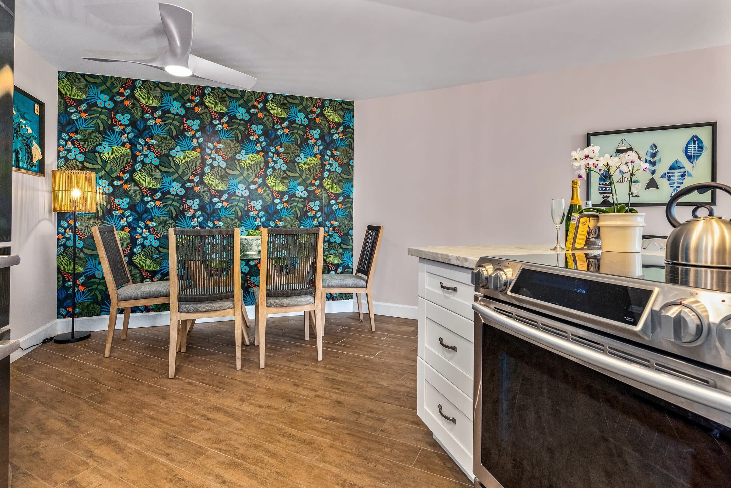 A modern kitchen with a wooden dining table, chairs, a built-in oven, and a decorative wall with a floral pattern.