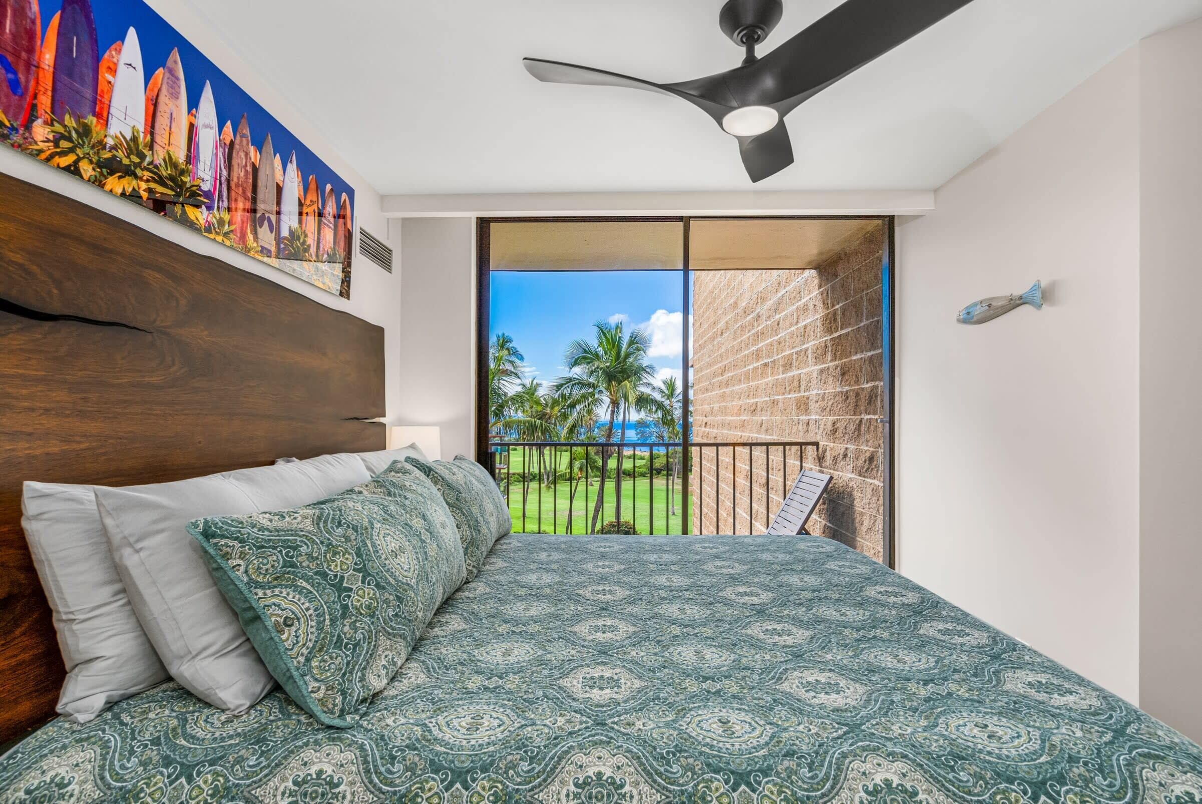 A bedroom with a bed, a ceiling fan, a view of a balcony with a railing, and a painting on the wall.