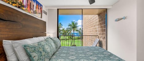 A bedroom with a bed, a ceiling fan, a view of a balcony with a railing, and a painting on the wall.