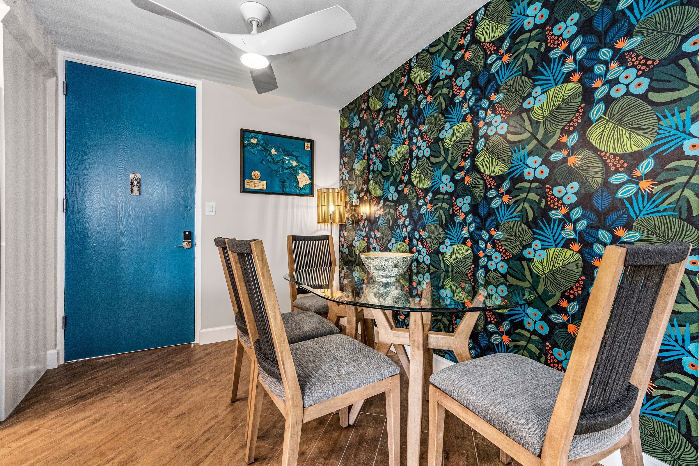 A dining area with a blue door, a wall with a floral pattern, and a ceiling fan.