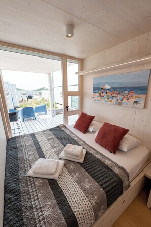 A bedroom with a large bed, a painting of a beach scene, and a view of the outdoor area.
