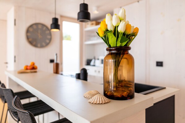 A kitchen counter with a vase of tulips, a seashell, and a clock on the wall.