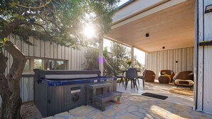 An outdoor patio area with a hot tub, stone flooring, wooden deck, and seating furniture.