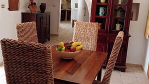 Un comedor con mesa de madera, sillas tejidas y una cesta de frutas.