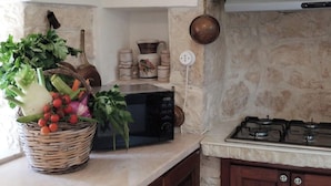 Una cocina con microondas, una cesta de verduras frescas, una estufa a gas y una pared de piedra.