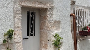 Pared blanca texturizada con una puerta que tiene una verja metálica y un ventanal pequeño.
