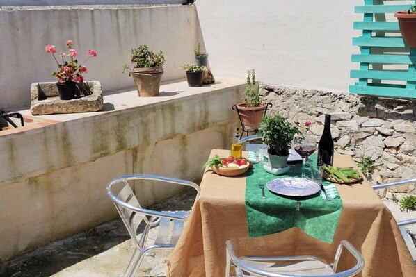 Una terraza en la azotea con una mesa lista para cenar, rodeada de plantas en macetas y una botella de vino.