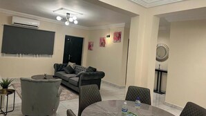 A modern living room with a sofa, armchairs, a dining table, and a ceiling light fixture. - 3 Bed Apartment Sleeps 6 - EnSuites, Parking, Wifi (Freetown)