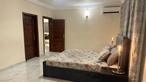A bedroom with a bed, a nightstand, a lamp, and a window with curtains. - 3 Bed Apartment Sleeps 6 - EnSuites, Parking, Wifi (Freetown)