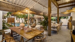 A spacious outdoor area with a wooden table, wicker chairs, a thatched-roof seating area, and a pool. - Villa Cyma by Alfred in Bali (Seminyak)