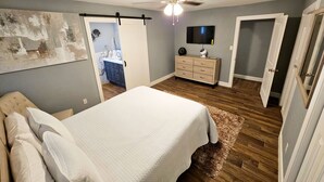 A bedroom with a bed, a dresser, a ceiling fan, a TV, and a door leading to another room. - Mama’s Modern House is family and pet friendly, large yard, quartz countertops  (Cypress)