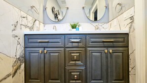 A bathroom with a dark wooden vanity, two round mirrors, and a marble backsplash. - Mama’s Modern House is family and pet friendly, large yard, quartz countertops  (Cypress)